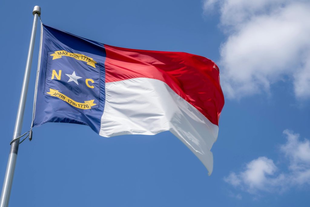 North Carolina state flag waving in the breeze with a clear blue sky backdrop.